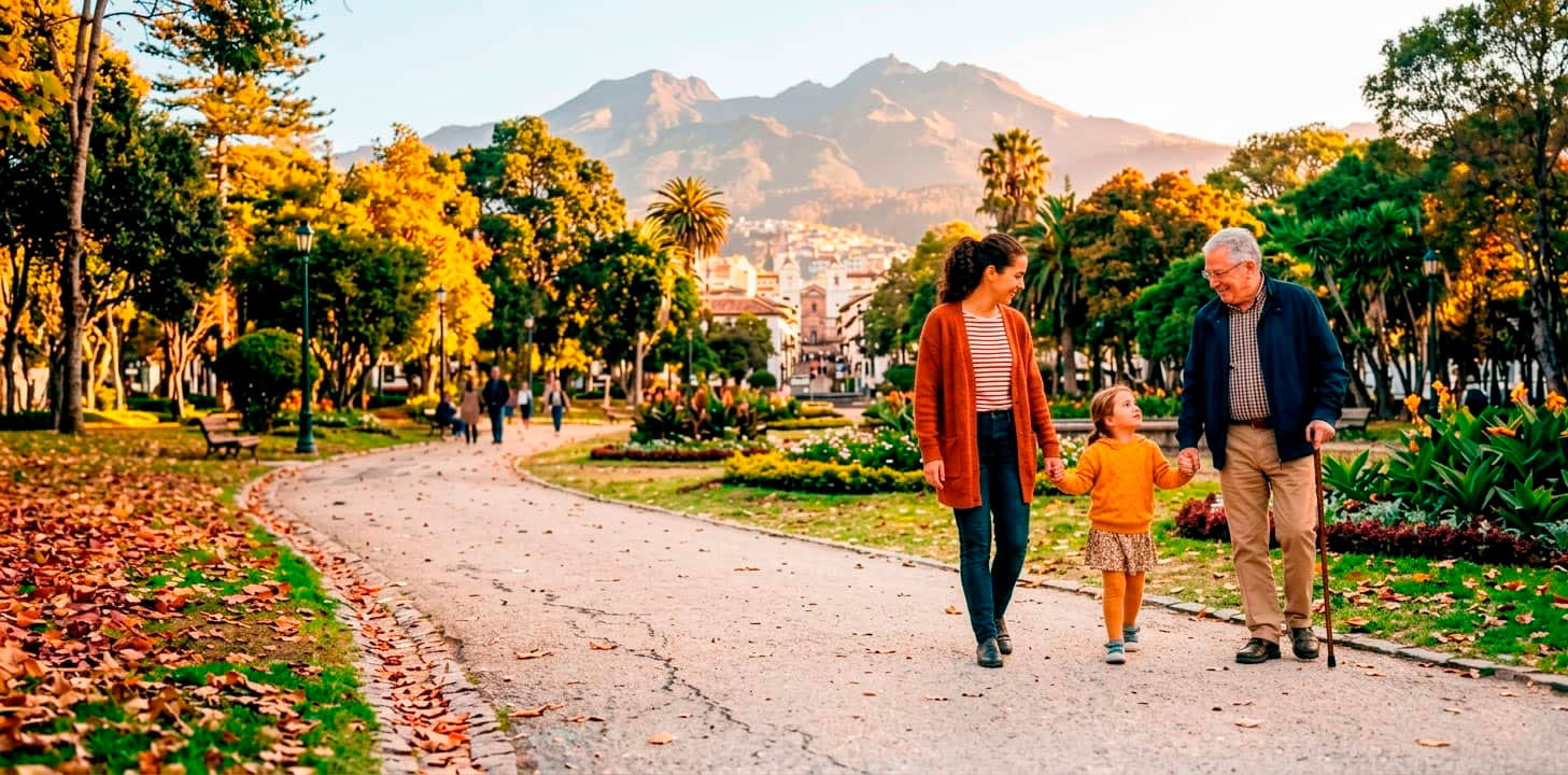 Familia paseando en parque con árboles y montañas al fondo, promoviendo sostenibilidad y salud.