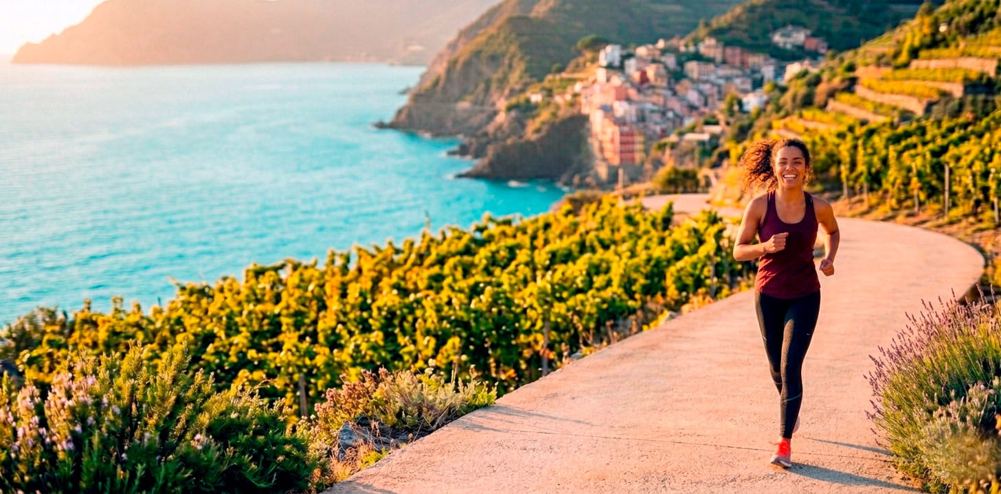 Mujer corriendo en un sendero costero con vistas al mar y montañas, promoviendo salud y bienestar.